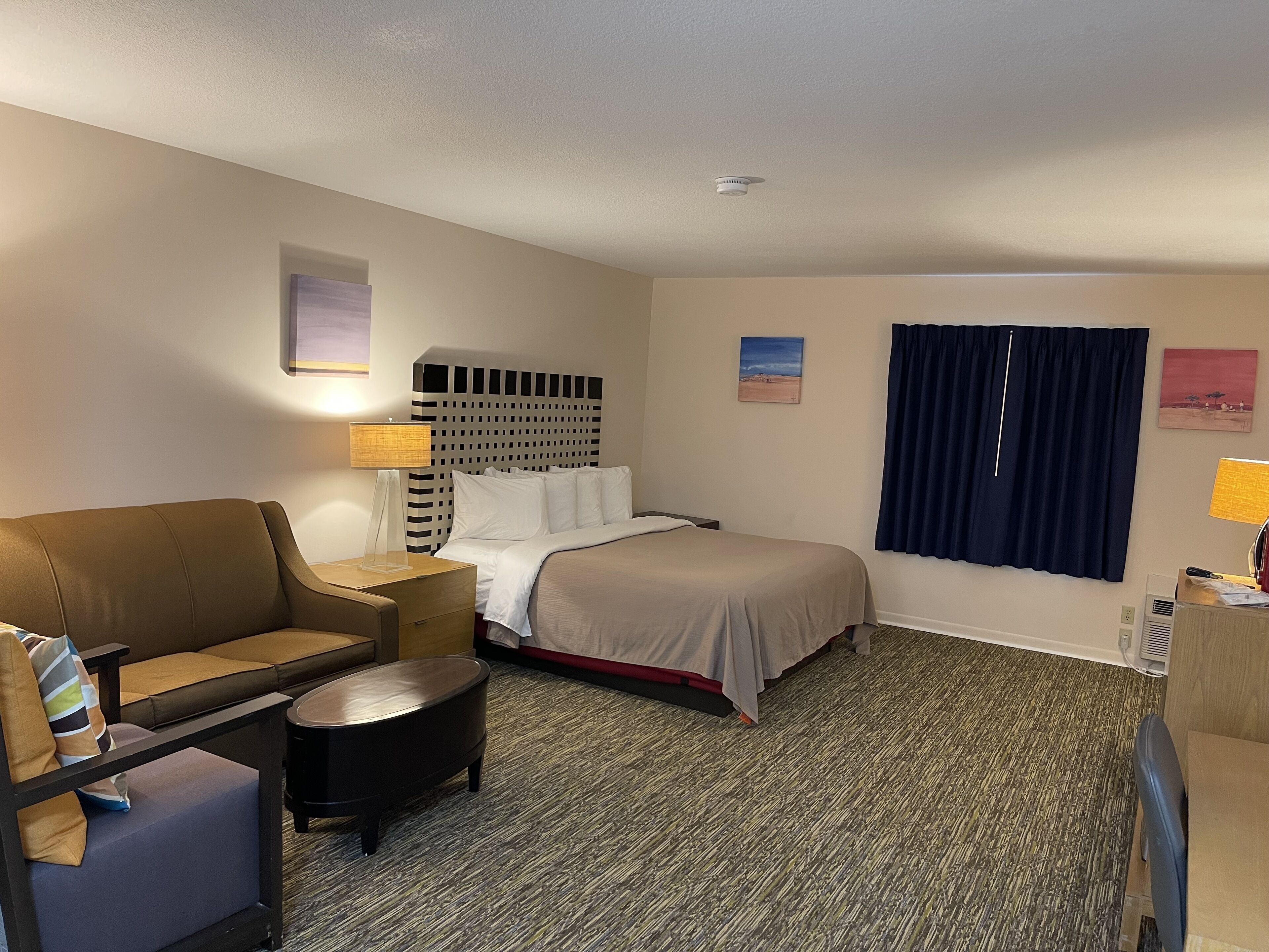 A hotel room with a bed, a sofa, a small table, a lamp, and a window with curtains.