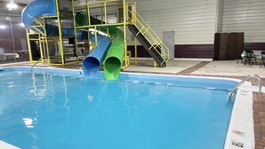 An indoor swimming pool with two slides, a staircase, and a covered seating area. - Rodeway Inn Oscoda (Oscoda)