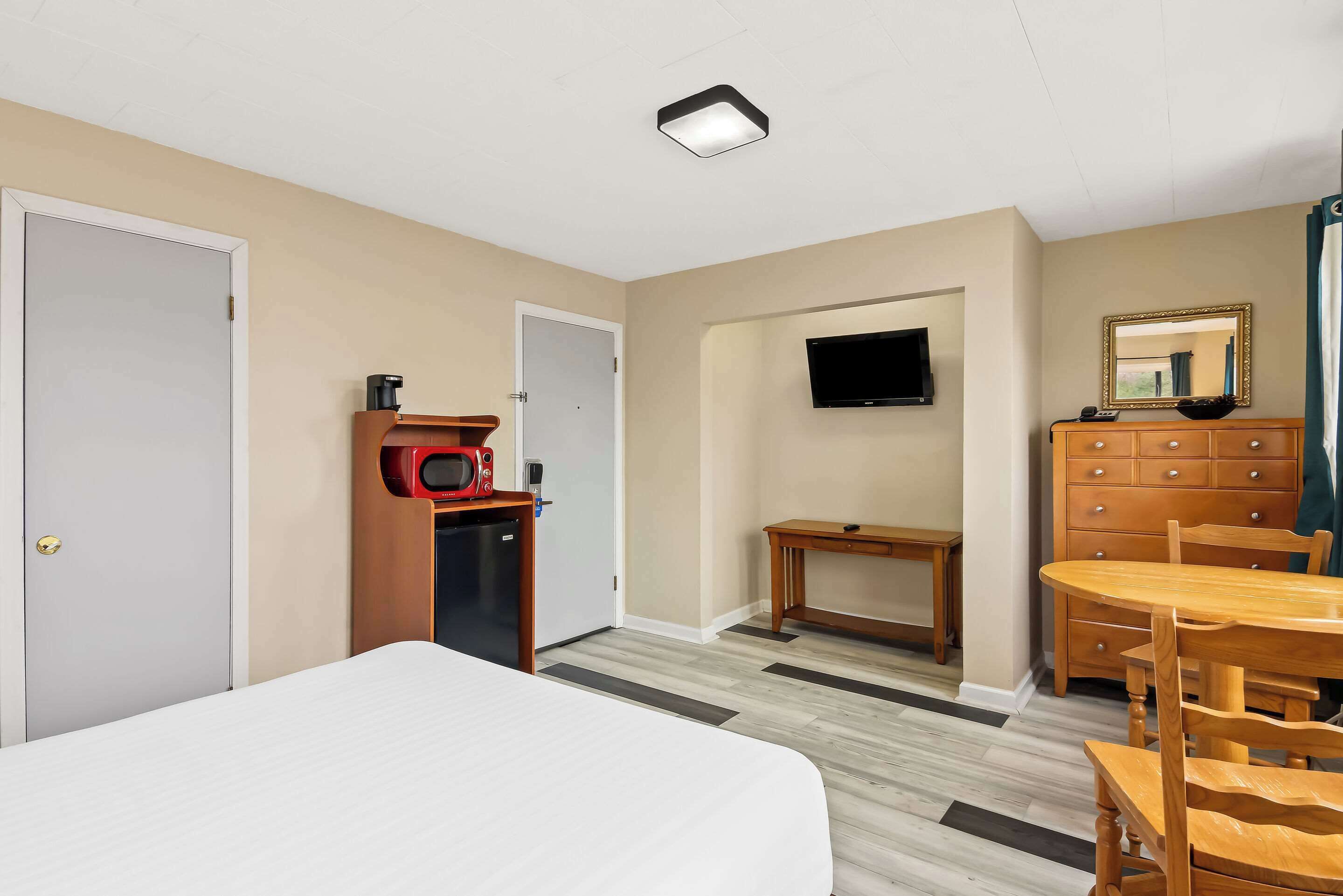 A hotel room with a bed, a desk with a chair, a dresser, a microwave, and a television.