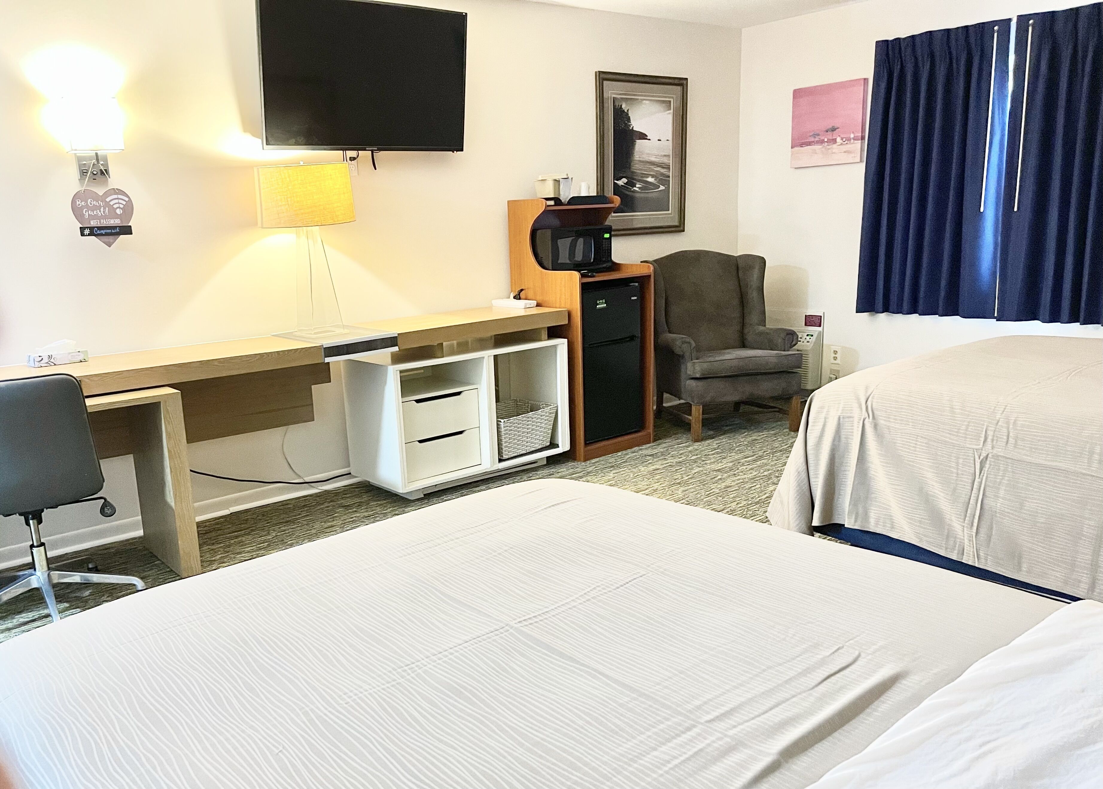 Une chambre d’hôtel équipée d’un lit, d’un bureau avec un ordinateur, d’une chaise, d’une télévision et d’un four à micro-ondes.