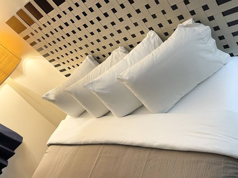 A neatly made bed with white linens and pillows, a woven headboard, and a lamp on the left.