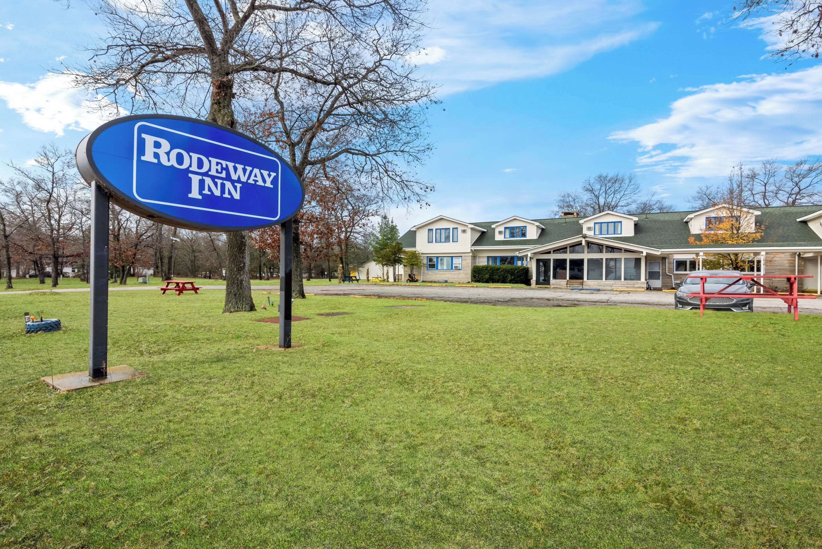 A sign for Rodeway Inn with a lawn and picnic table in the foreground.