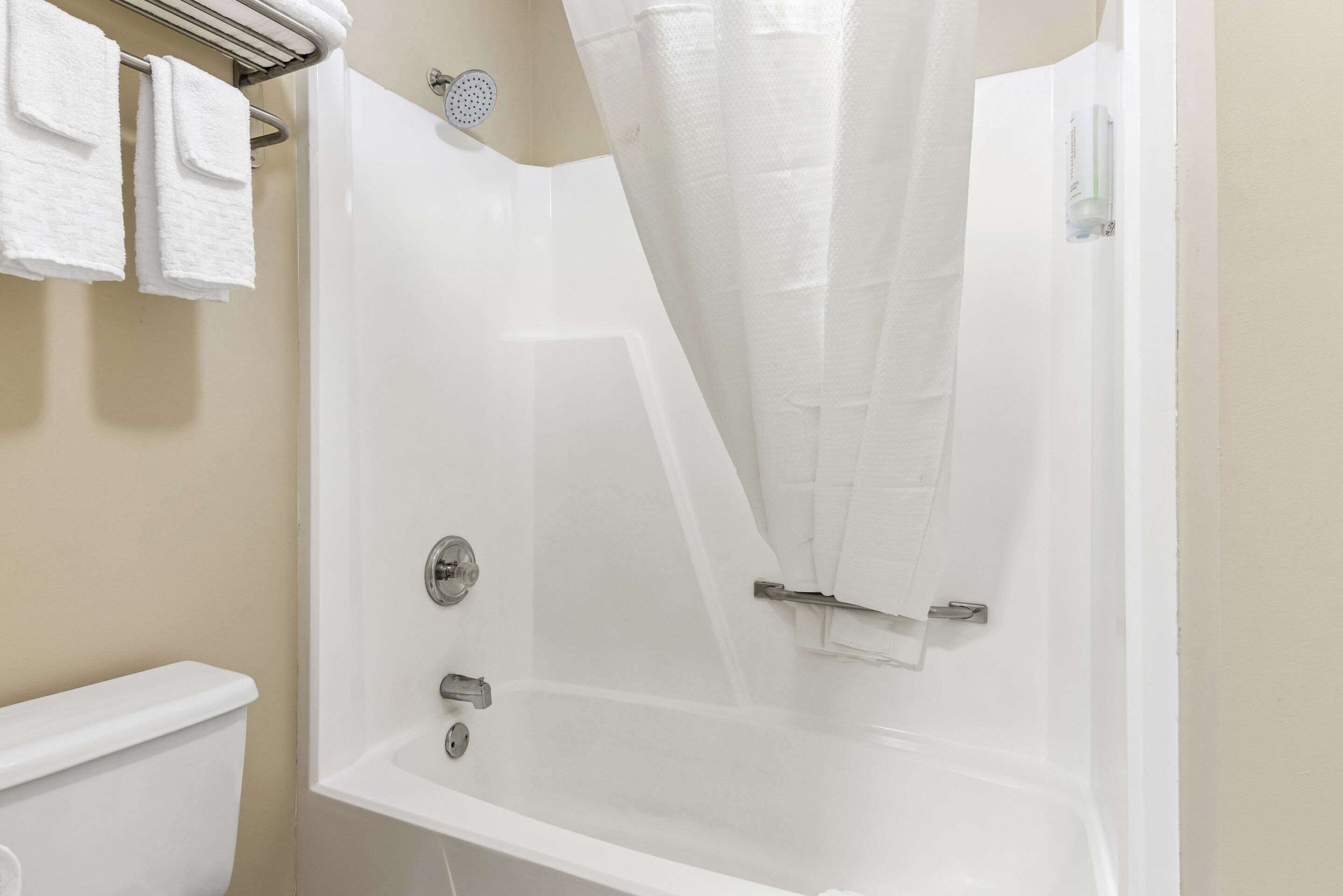 A white bathtub with a shower curtain, a towel rack with white towels, and a toilet.