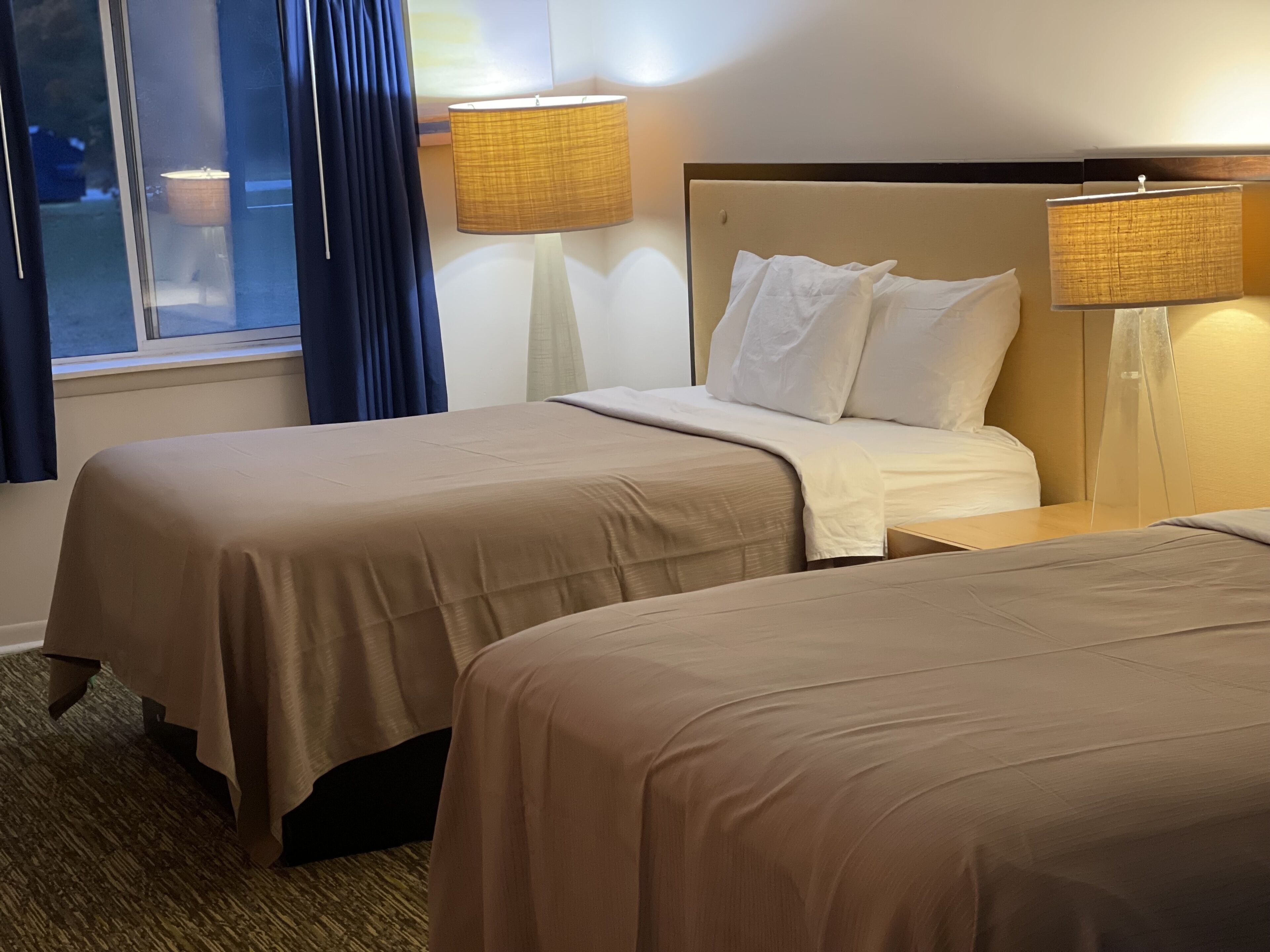 Una habitación de hotel con dos camas, una ventana con cortinas y dos lámparas fijadas a la pared.