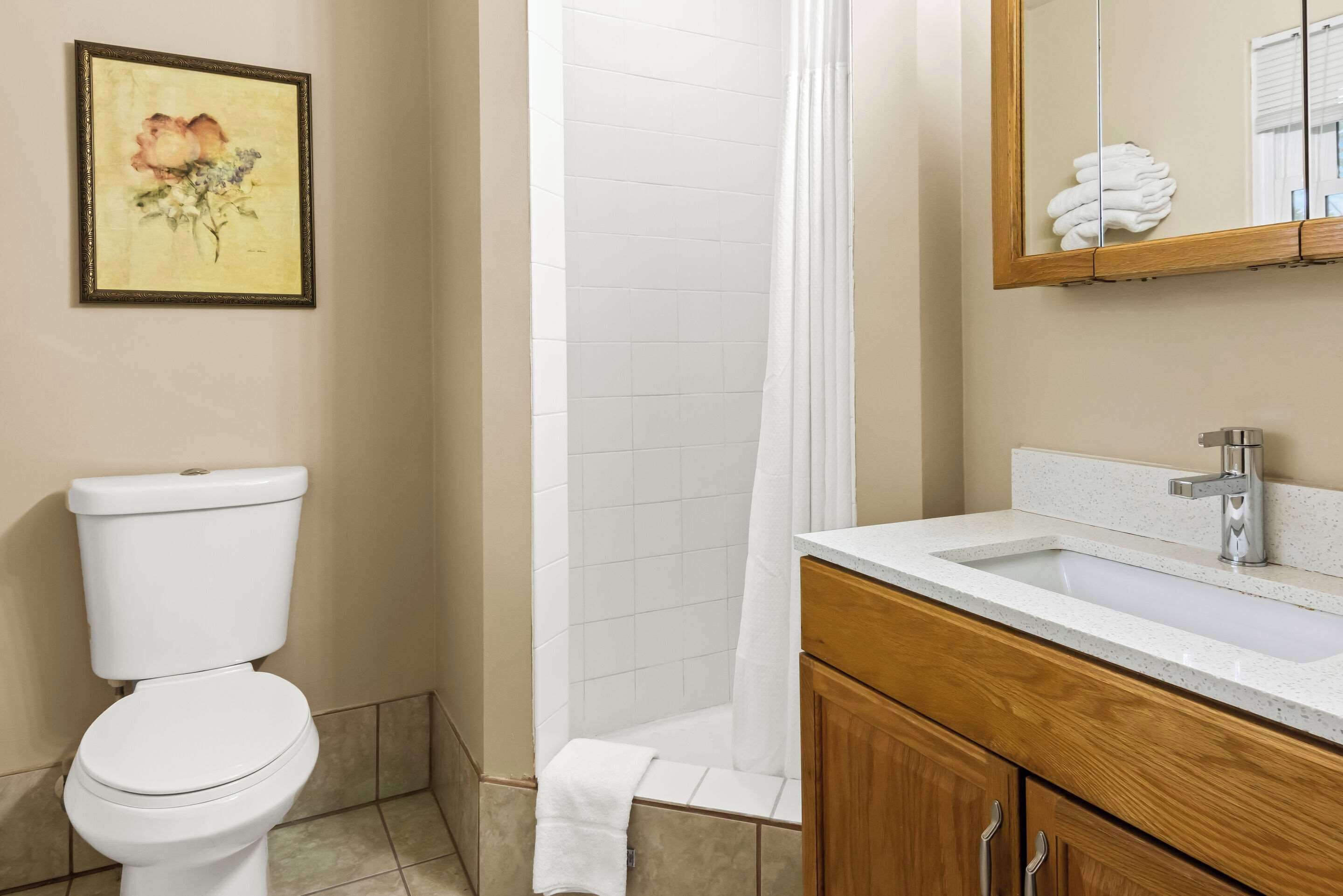 A bathroom with a toilet, shower, sink, and wooden vanity.