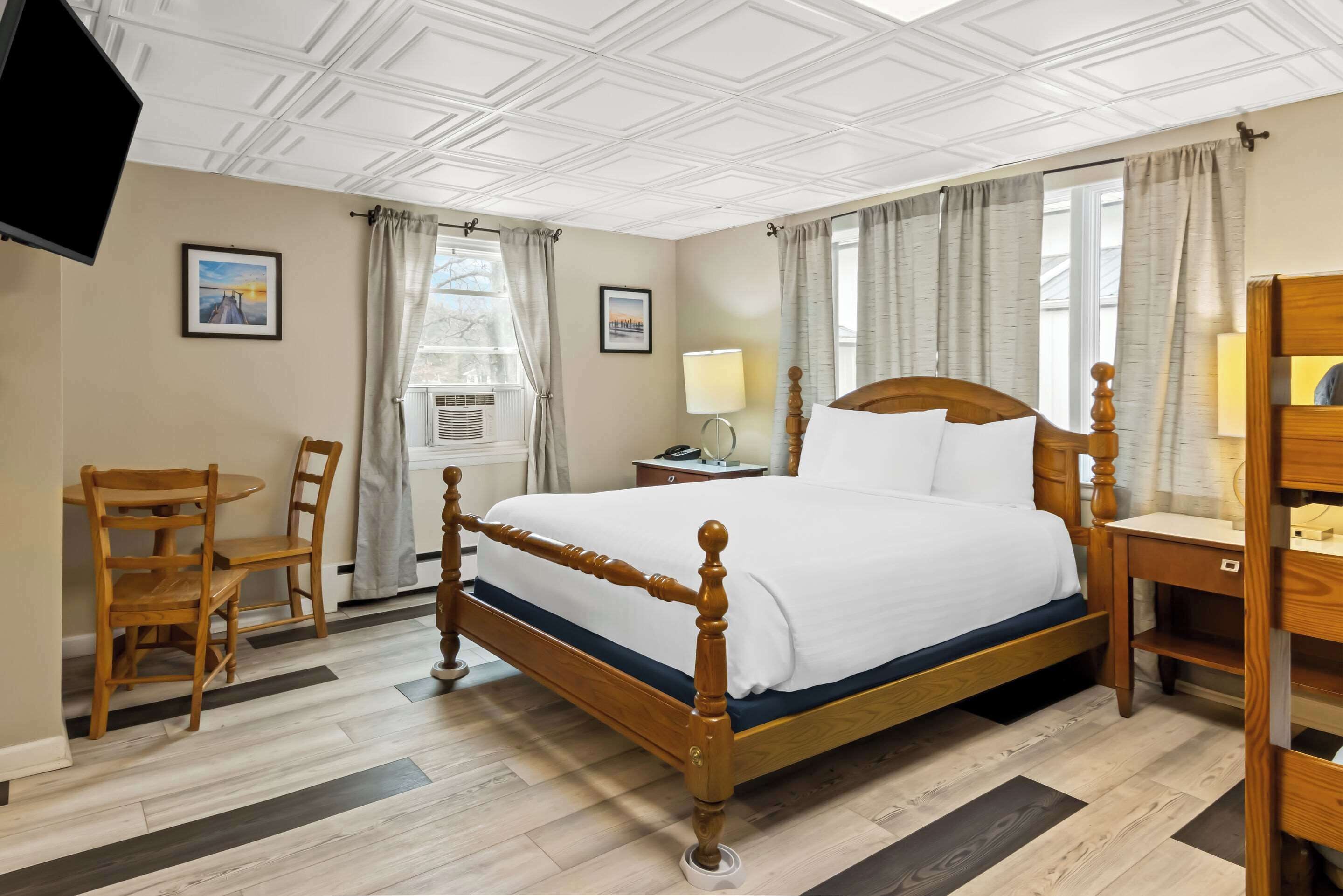 A neatly arranged bedroom with a wooden bed, a bedside table, a chair, and a TV mounted on the wall.