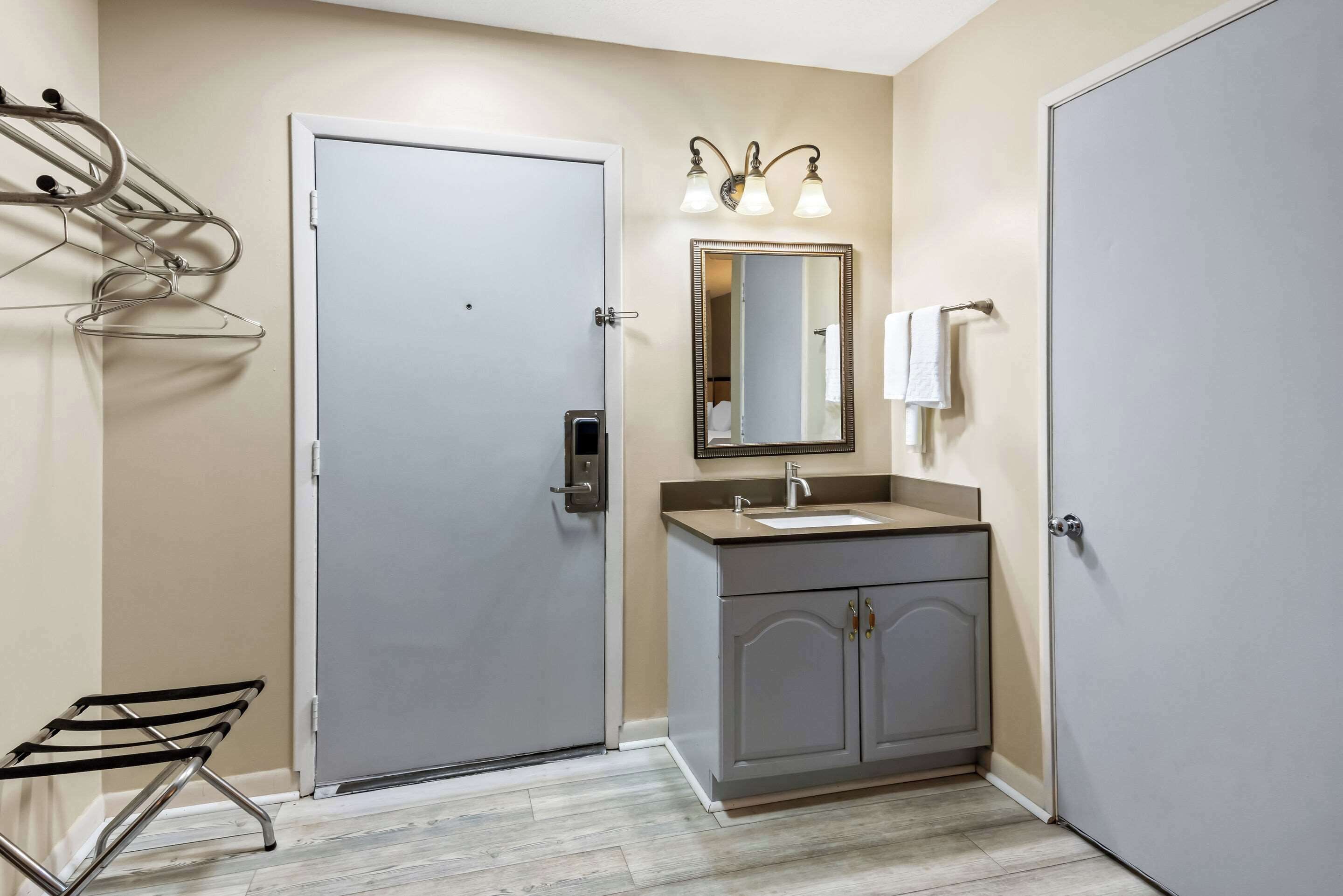 A bathroom with a door, a sink, a mirror, and a towel rack.