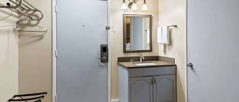 A bathroom with a door, a sink, a mirror, and a towel rack.