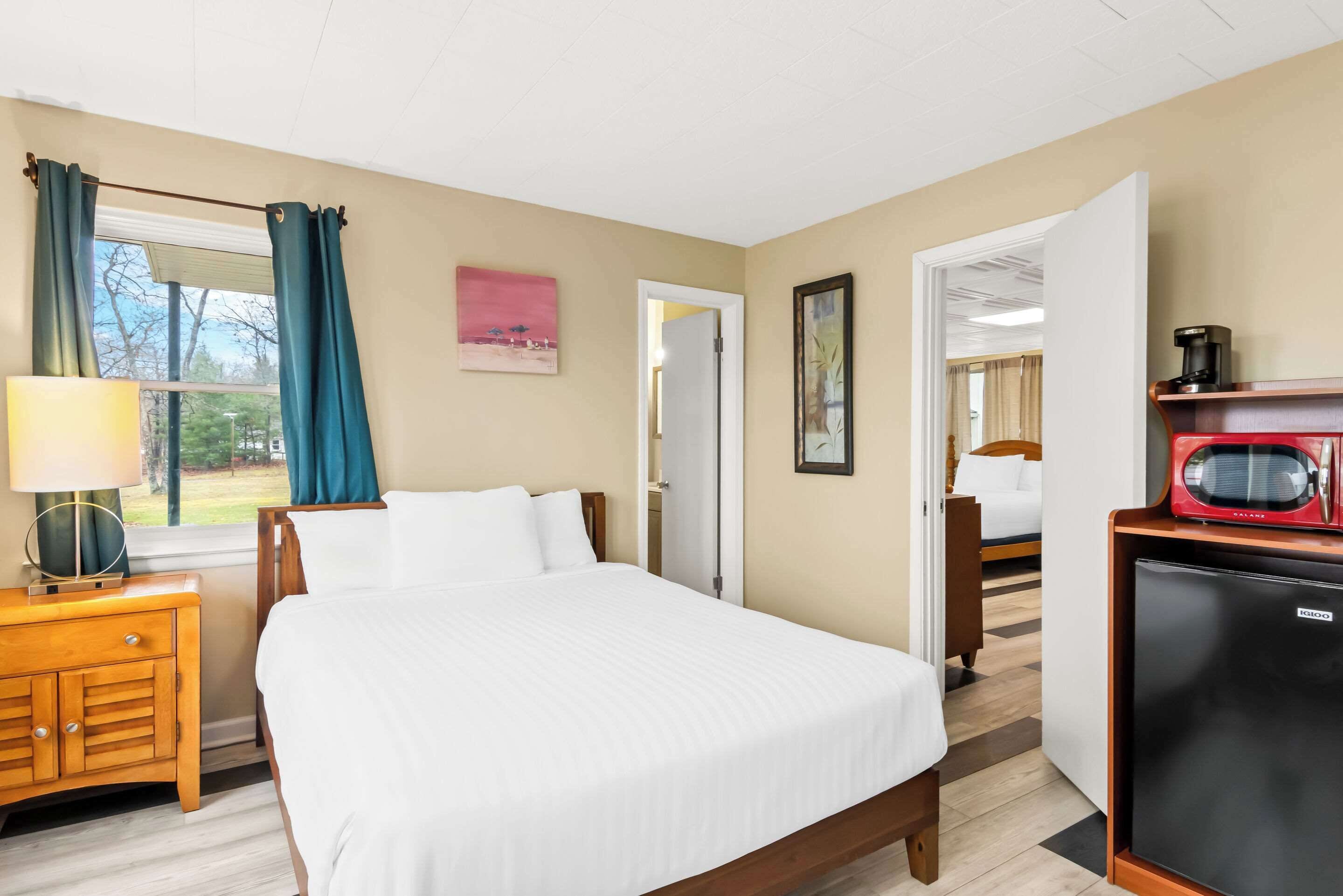 A hotel room with a bed, a nightstand, a desk, a refrigerator, and a window with curtains.