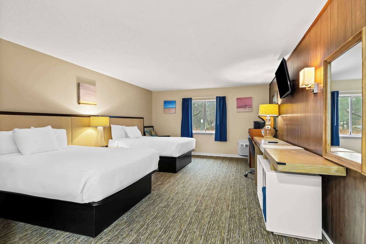 Quarto de hotel com duas camas, uma escrivaninha, televisão e obras de arte nas paredes.