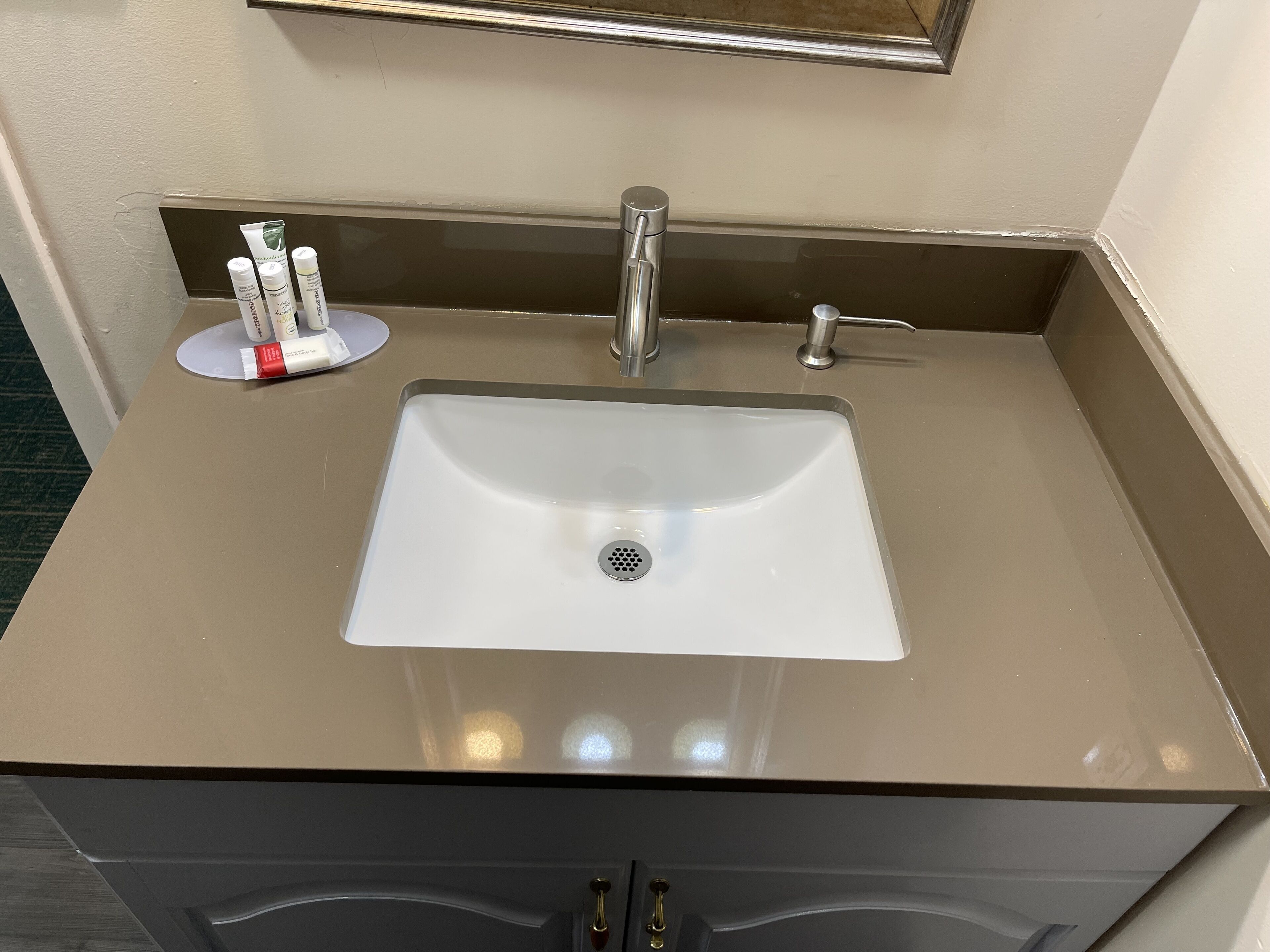 A bathroom sink with a mirror above it, a faucet, and a small shelf with toiletries.