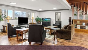 A spacious living room with a flat-screen TV, comfortable seating, a fireplace, and a staircase. - Rodeway Inn Oscoda (Oscoda)