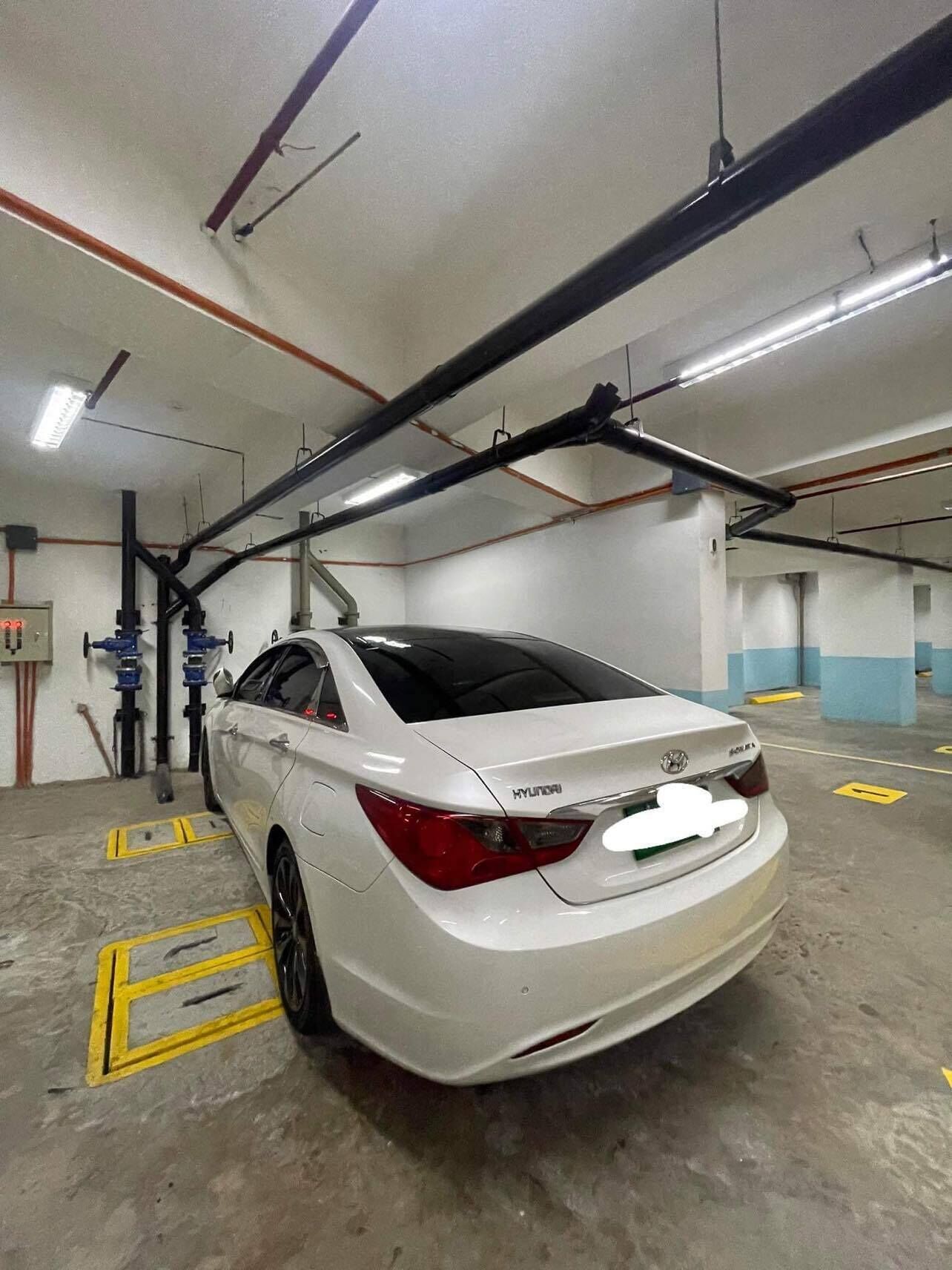 Un coche blanco Hyundai estacionado en un garaje subterráneo con suelos de hormigón e iluminación superior.