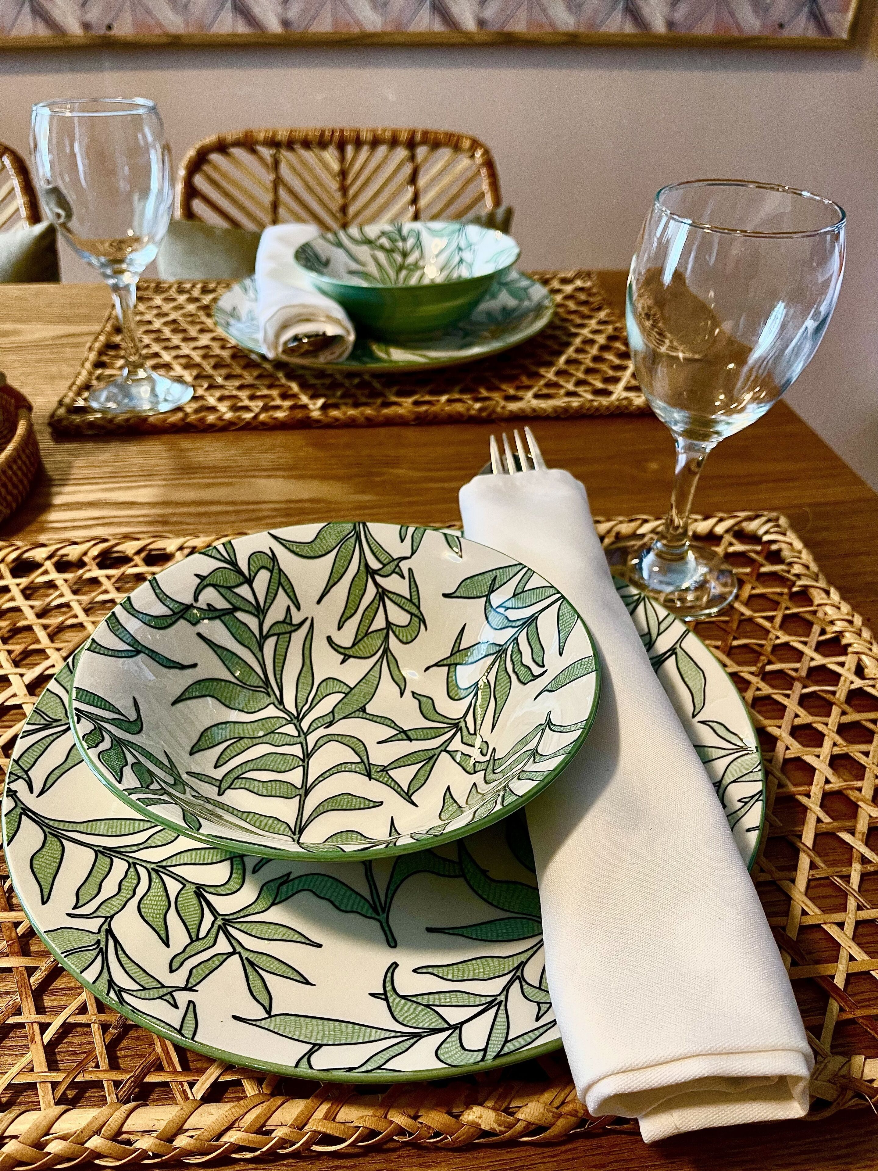 Una mesa de comedor dispuesta con dos platos, dos vasos y un servilleta doblada.