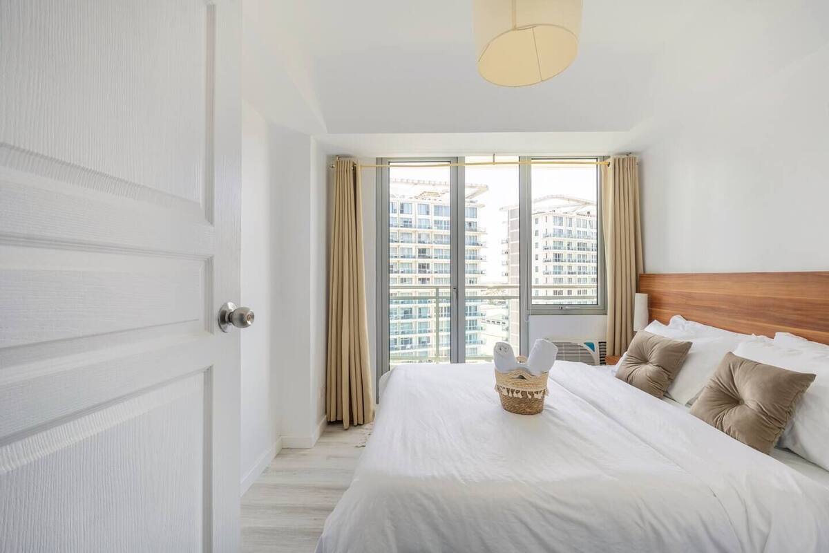 A hotel room with a large bed, a wooden headboard, and a view of high-rise buildings through the window.