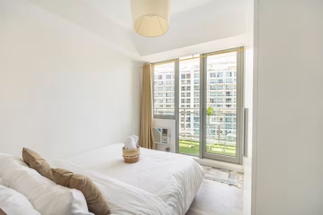 A hotel room with a large bed, a window with a view of high-rise buildings, and a ceiling light.