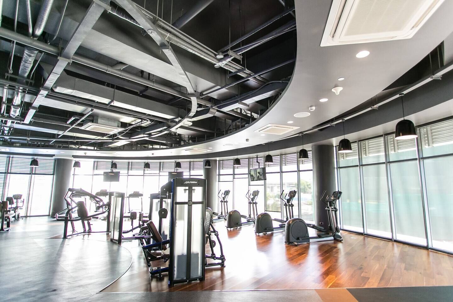 Een moderne sportschool met diverse fitnessapparaten, grote ramen en een gebogen plafond.