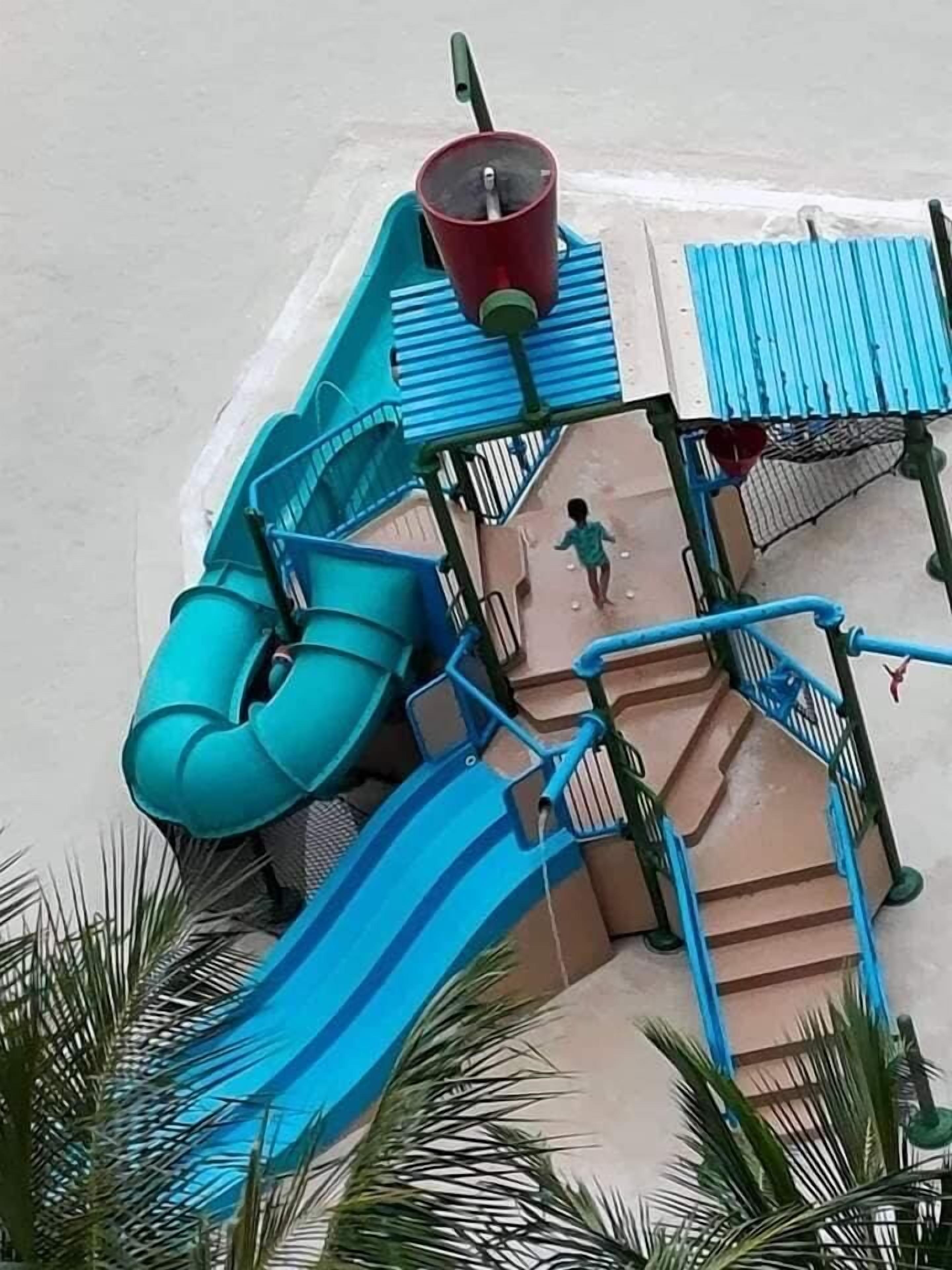 Parque acuático con un tobogán azul, un vaso rojo y una persona caminando.