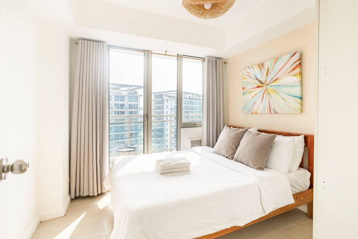 A modern hotel room with a large bed, a view of the city, and a colorful abstract painting on the wall.