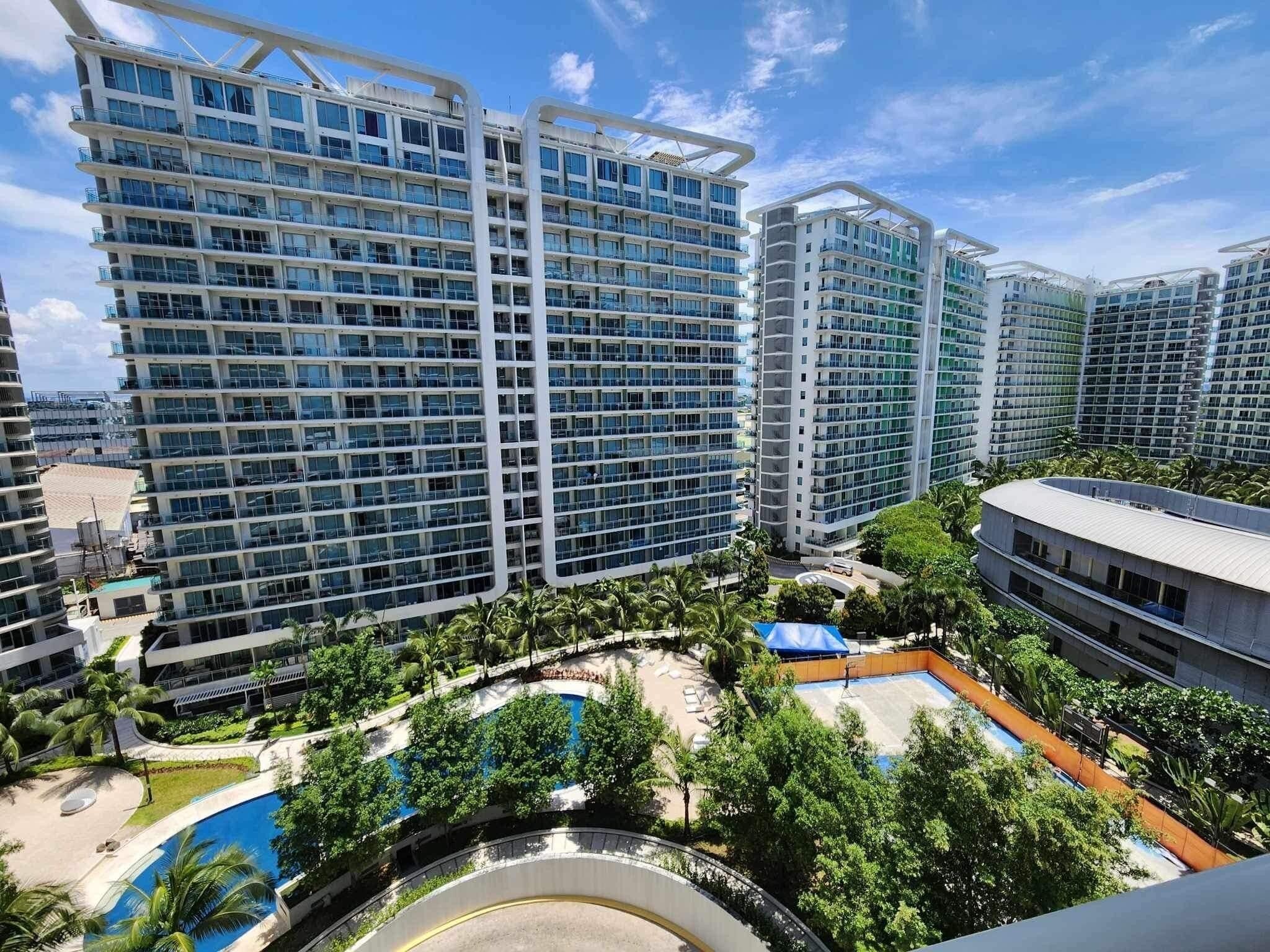 A high-rise residential building complex with multiple balconies, a swimming pool, and lush greenery.