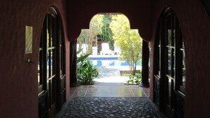 A corridor with a tiled floor leading to a pool area, surrounded by greenery and a blue building. - Paraíso Escondido (Jacó)
