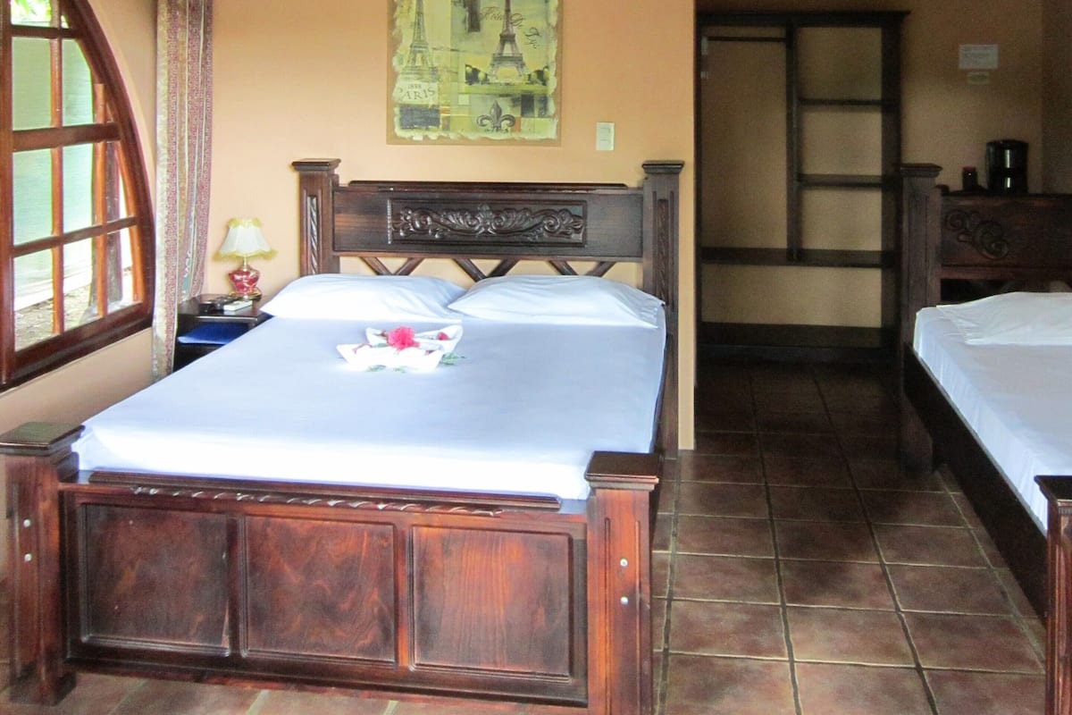 A bedroom with a large bed, a nightstand, a lamp, and a wall-mounted air conditioner.