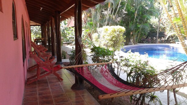 A covered patio with a pool, wooden chairs, and a hammock. - Paraíso Escondido (Jacó)