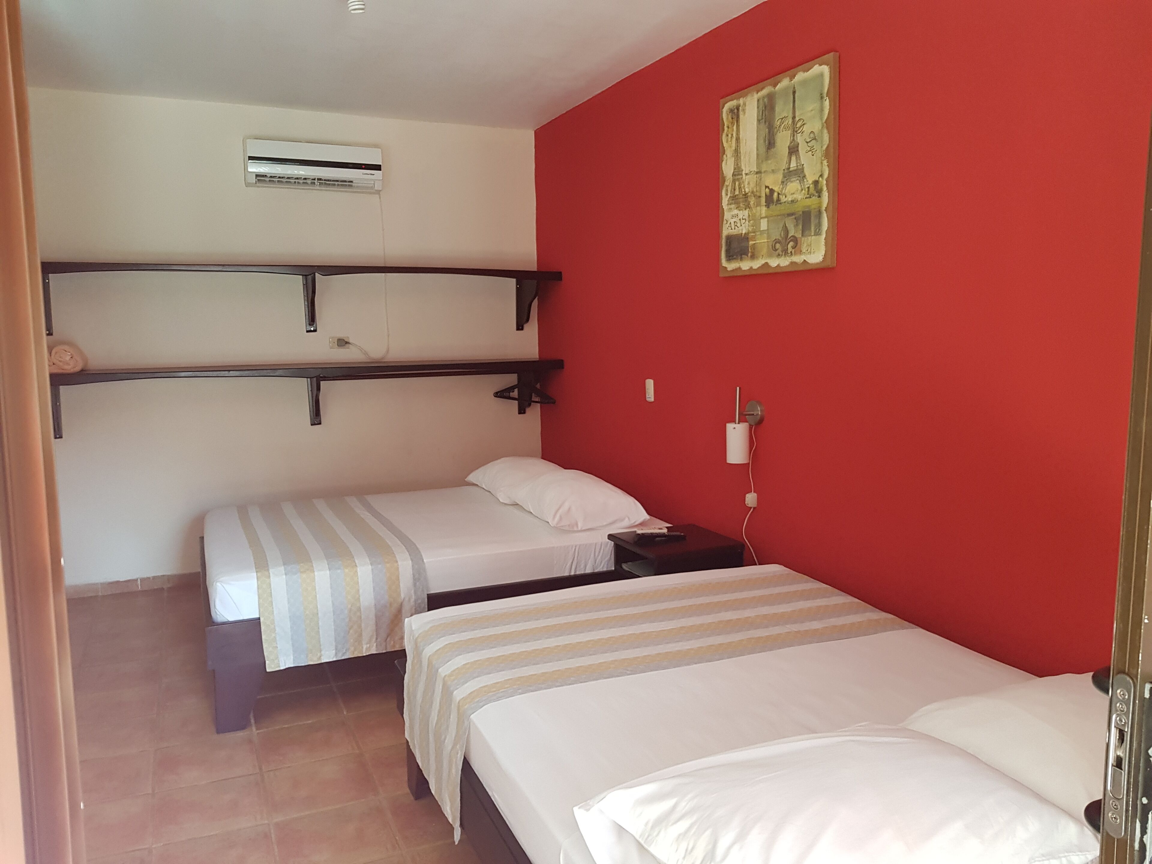 A room with two beds, a red wall, and a painting of the Eiffel Tower.