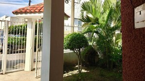 Uma entrada com portão, telhado de telhas vermelhas, uma pequena palmeira e um muro de concreto.