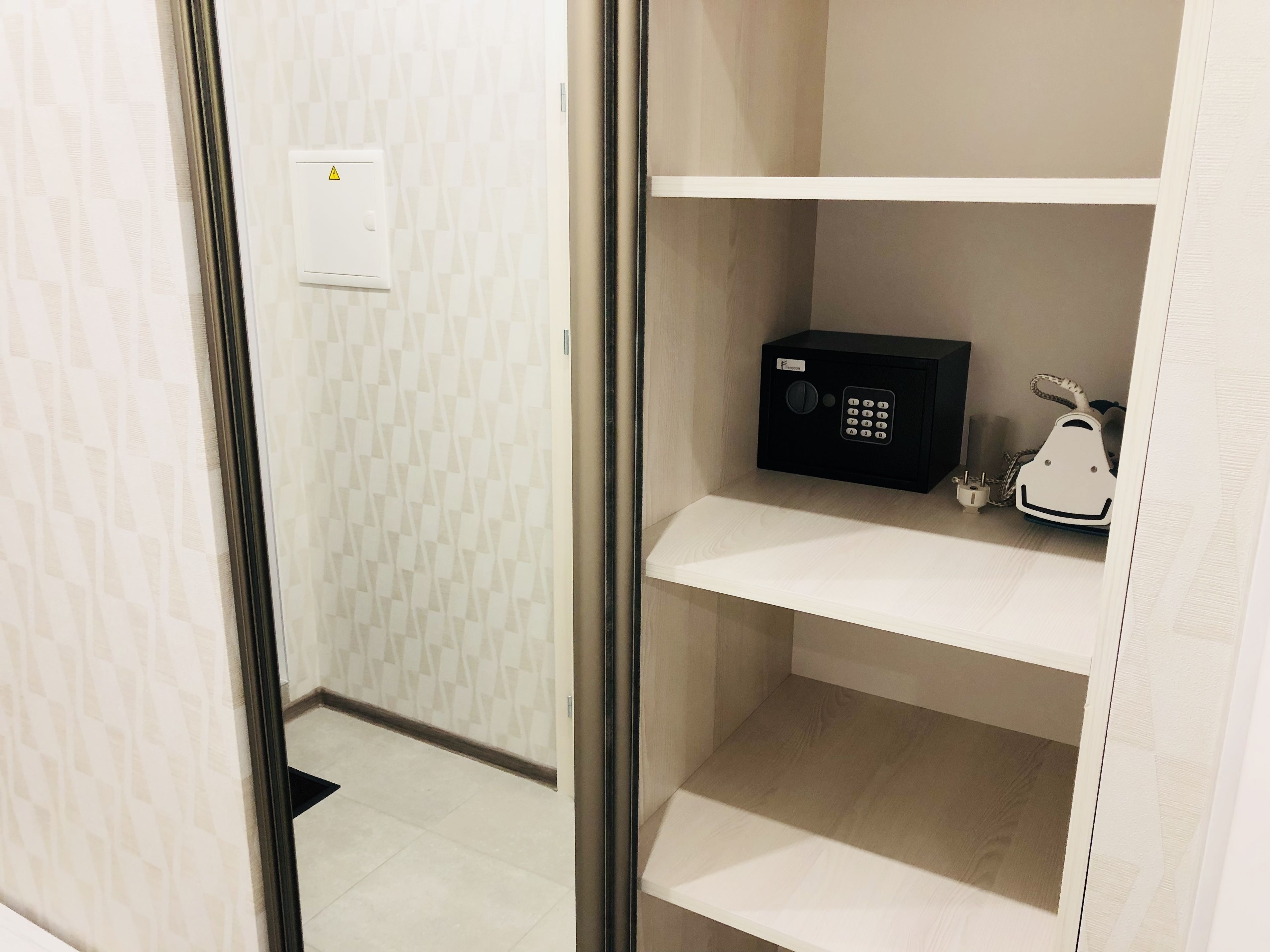 Una habitación de hotel con minibar, un enchufe y un pequeño electrodoméstico blanco en la estantería.