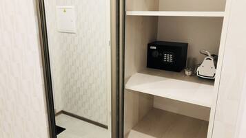 Una habitación de hotel con minibar, un enchufe y un pequeño electrodoméstico blanco en la estantería.