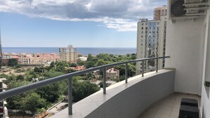 Un balcón con barandilla metálica que da a una zona residencial con diversos edificios y vistas al mar.