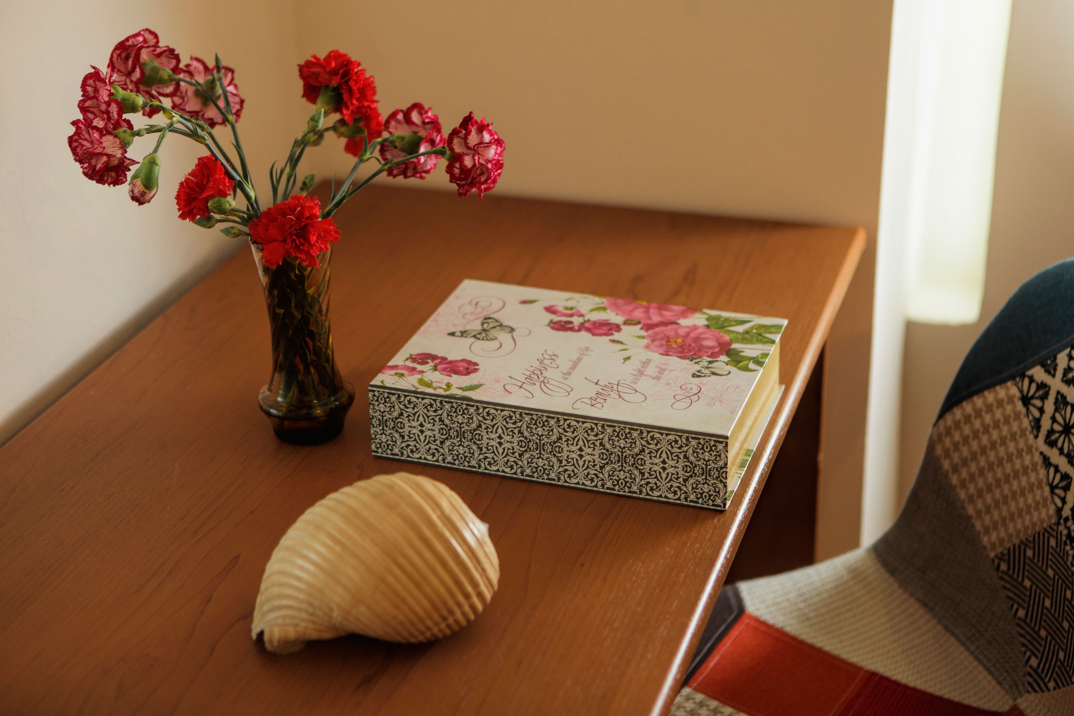 A wooden table with a vase of red flowers, a decorative box, and a seashell.