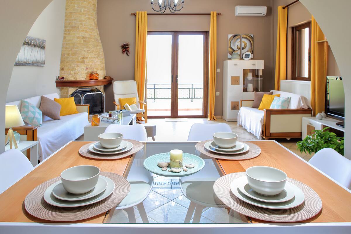 A modern hotel room with a dining area, a fireplace, and a balcony with yellow curtains.
