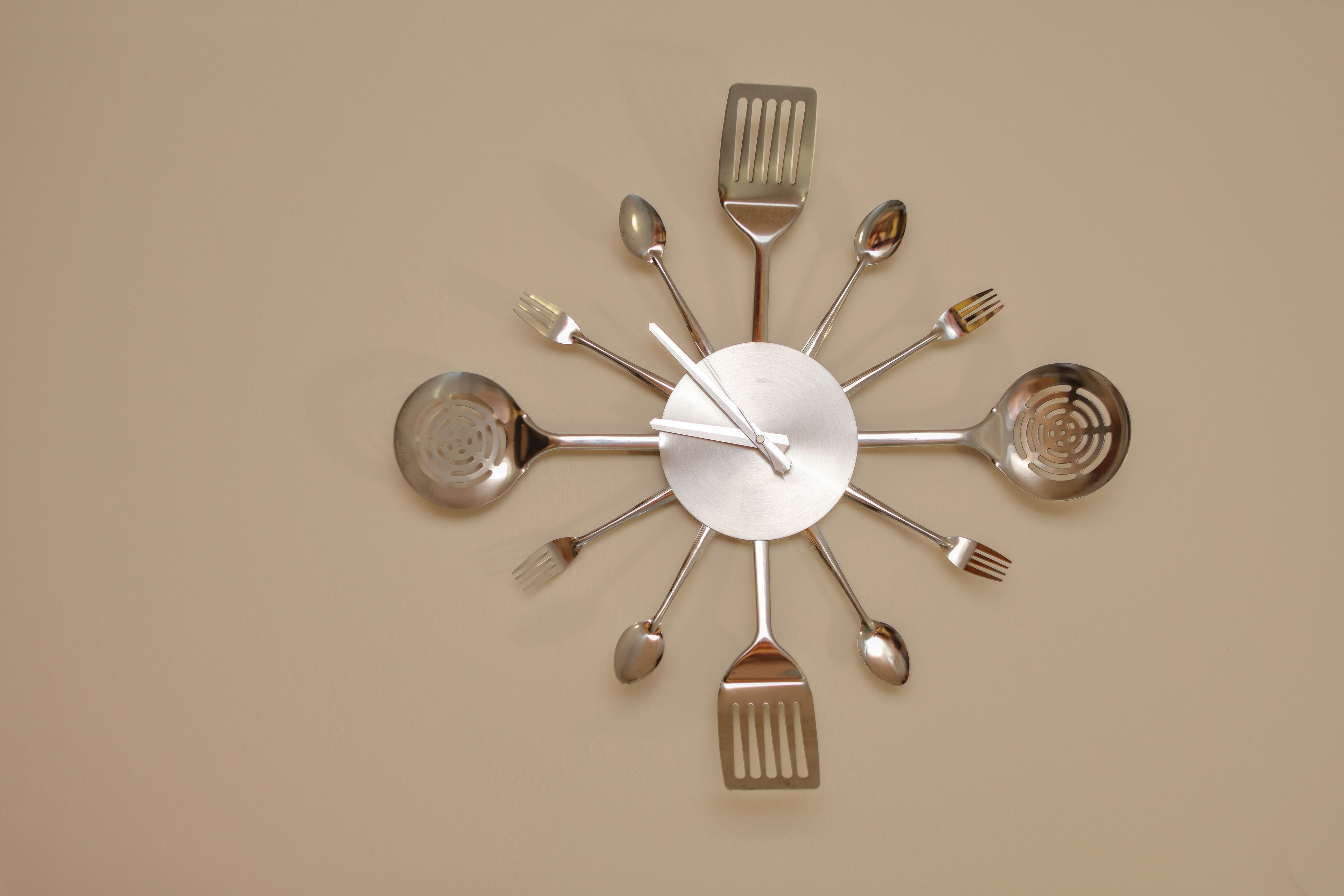 A wall clock with multiple spoons, forks, and spatulas as hour and minute hands.