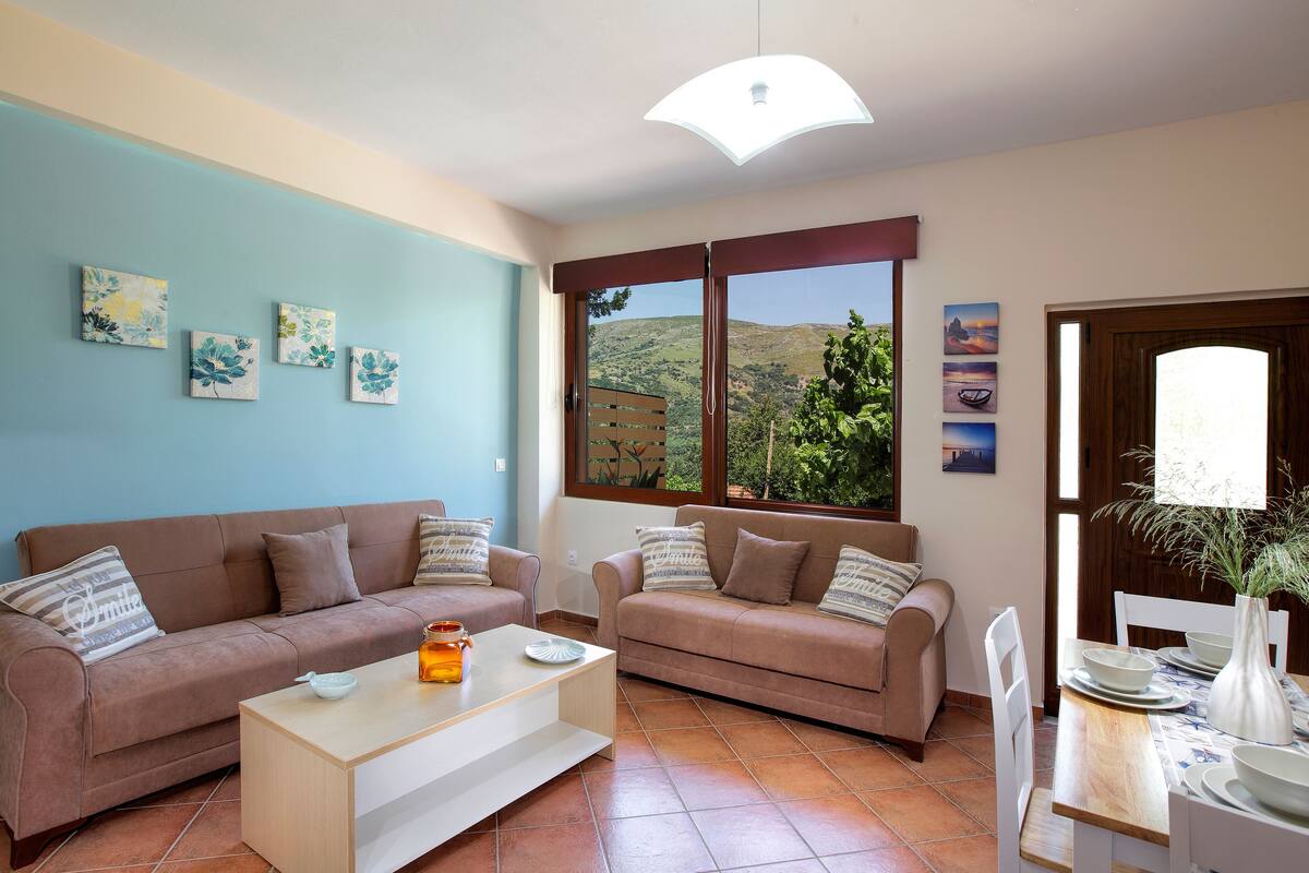A living room with two sofas, a coffee table, and a dining table set with plates and a vase.