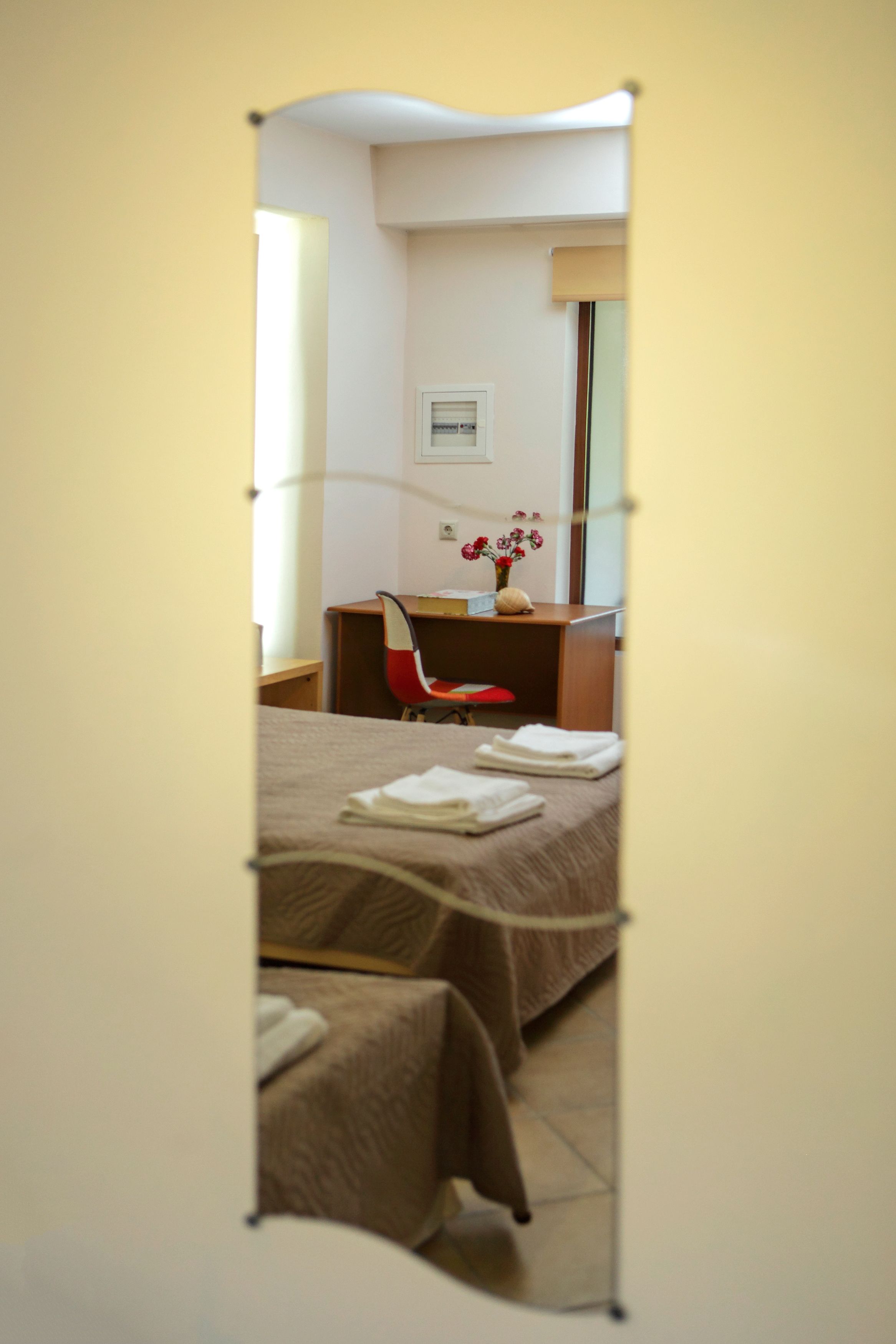 A hotel room with two beds, a desk, a chair, and a vase with flowers.