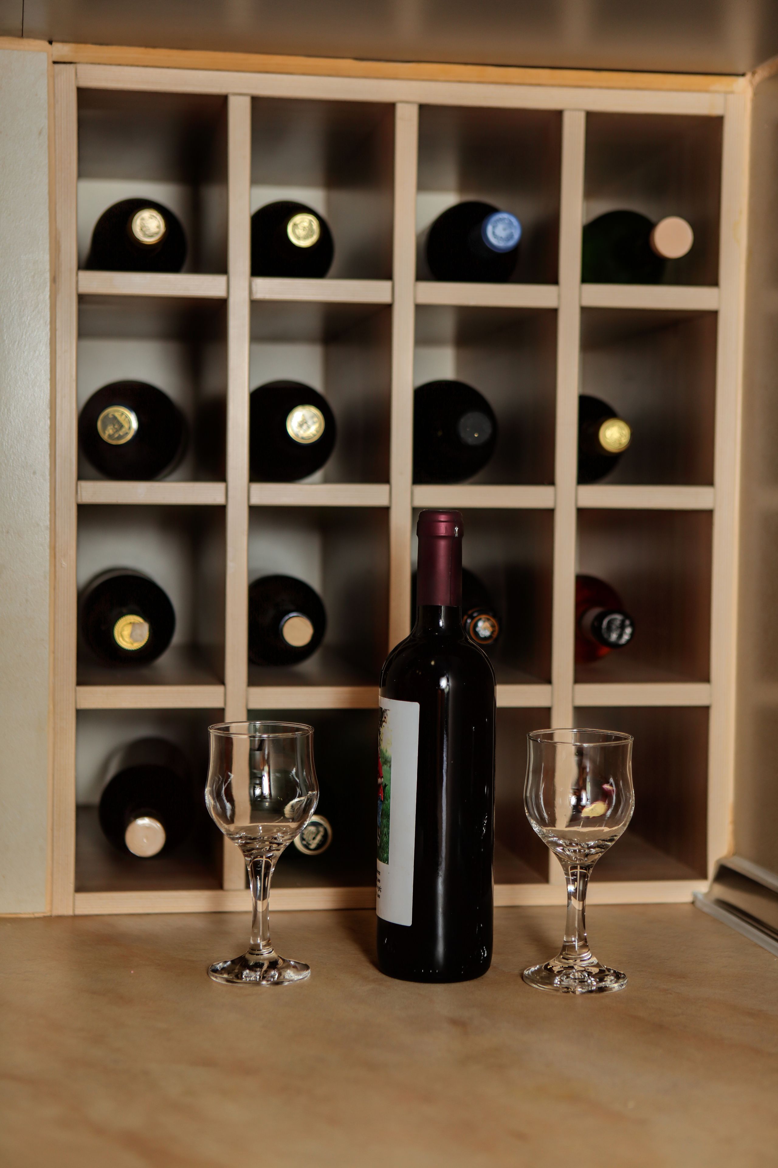 A wine rack with multiple bottles and two empty wine glasses.