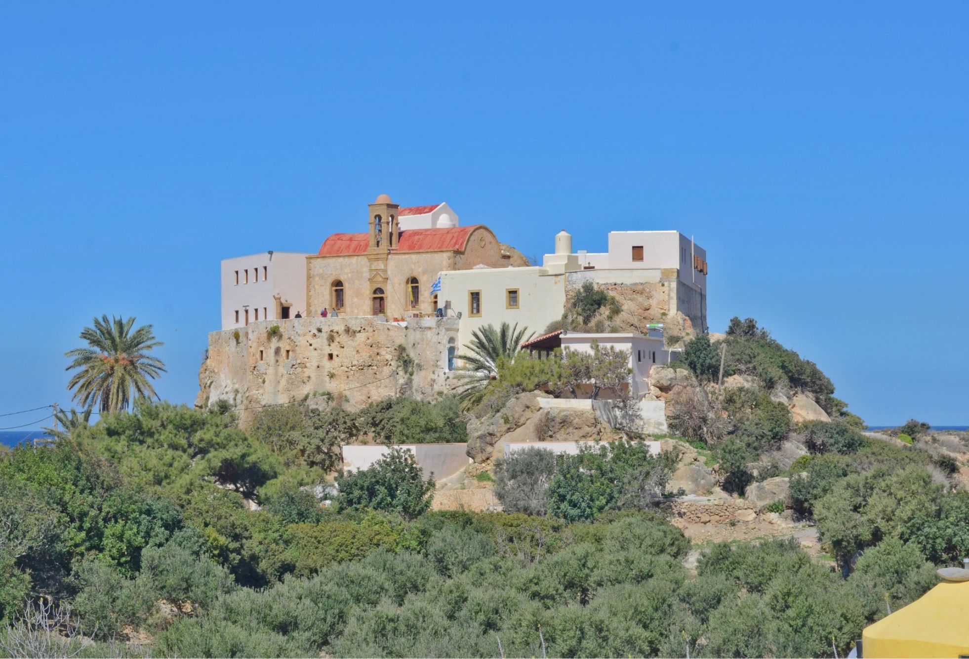 A historic building with a red roof, situated on a hill surrounded by greenery.