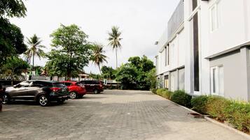 A paved driveway leading to a building with parked cars and palm trees in the background.