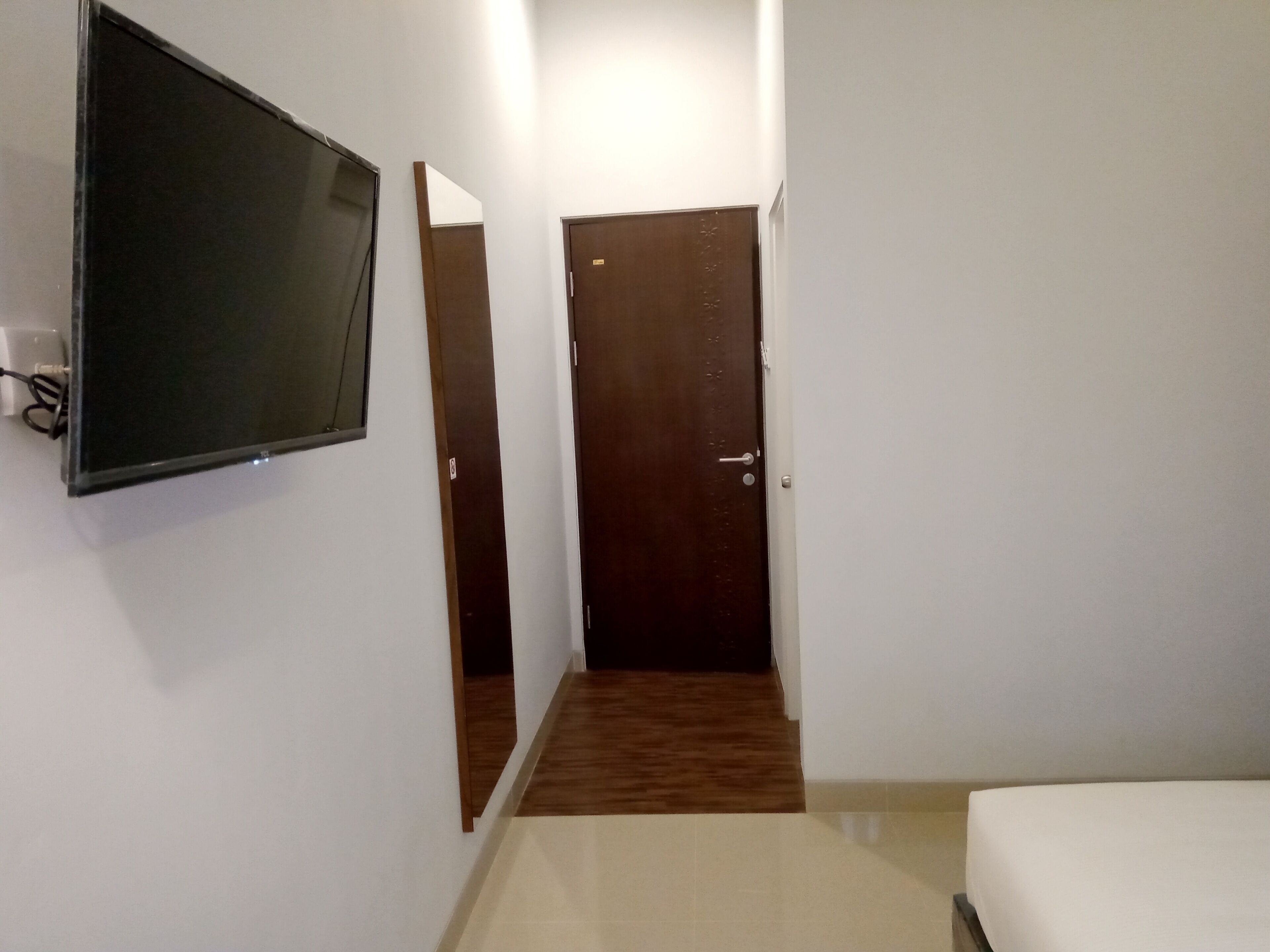 Habitació d'hotel amb televisió penjada a la paret, una porta de fusta i un paviment de rajoles.