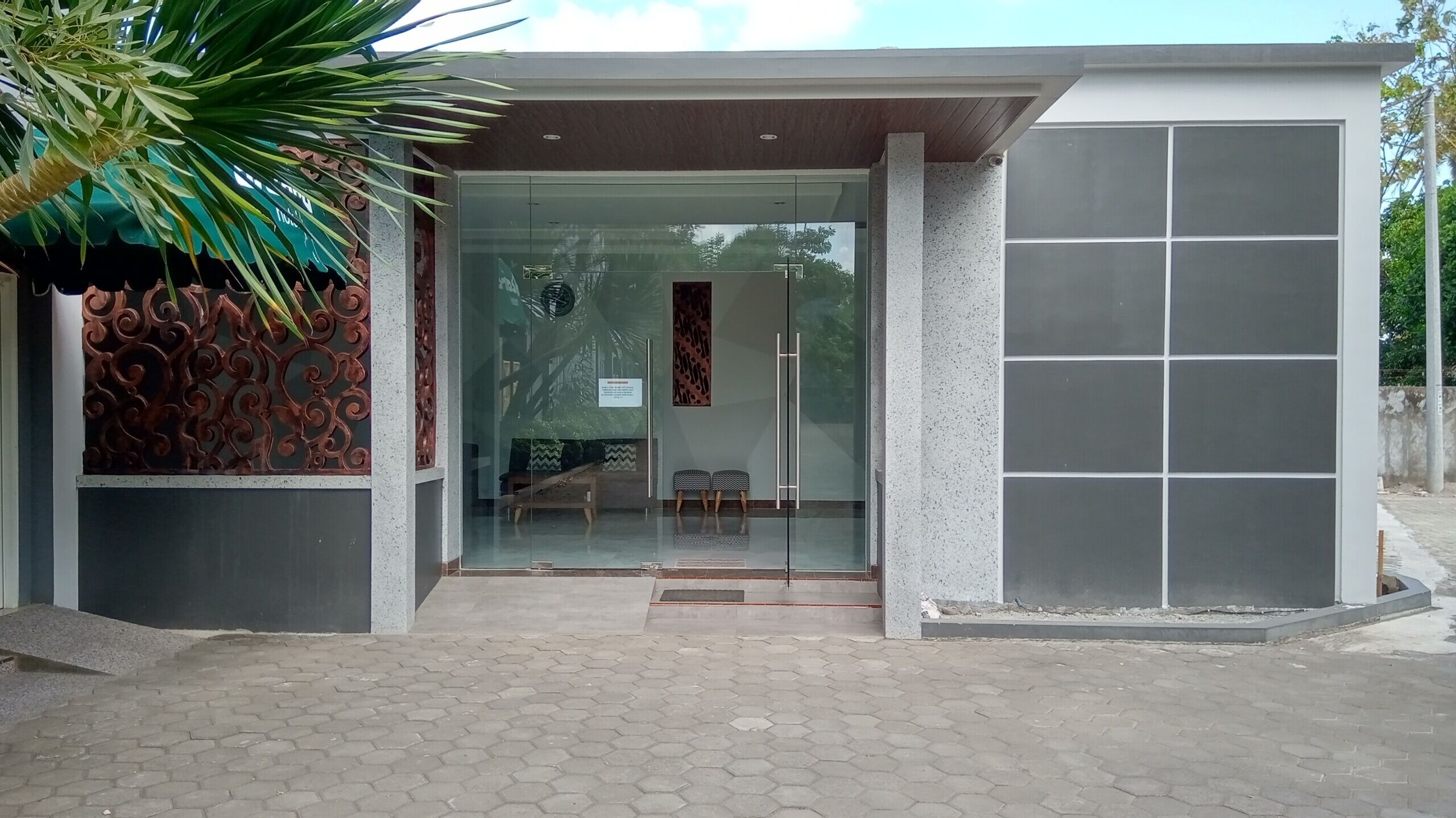 A modern building entrance with a glass door, a metal decorative wall, and a tiled pavement.