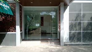 Entrada de hotel con puerta de cristal, una reja decorativa de metal y suelo de baldosas.