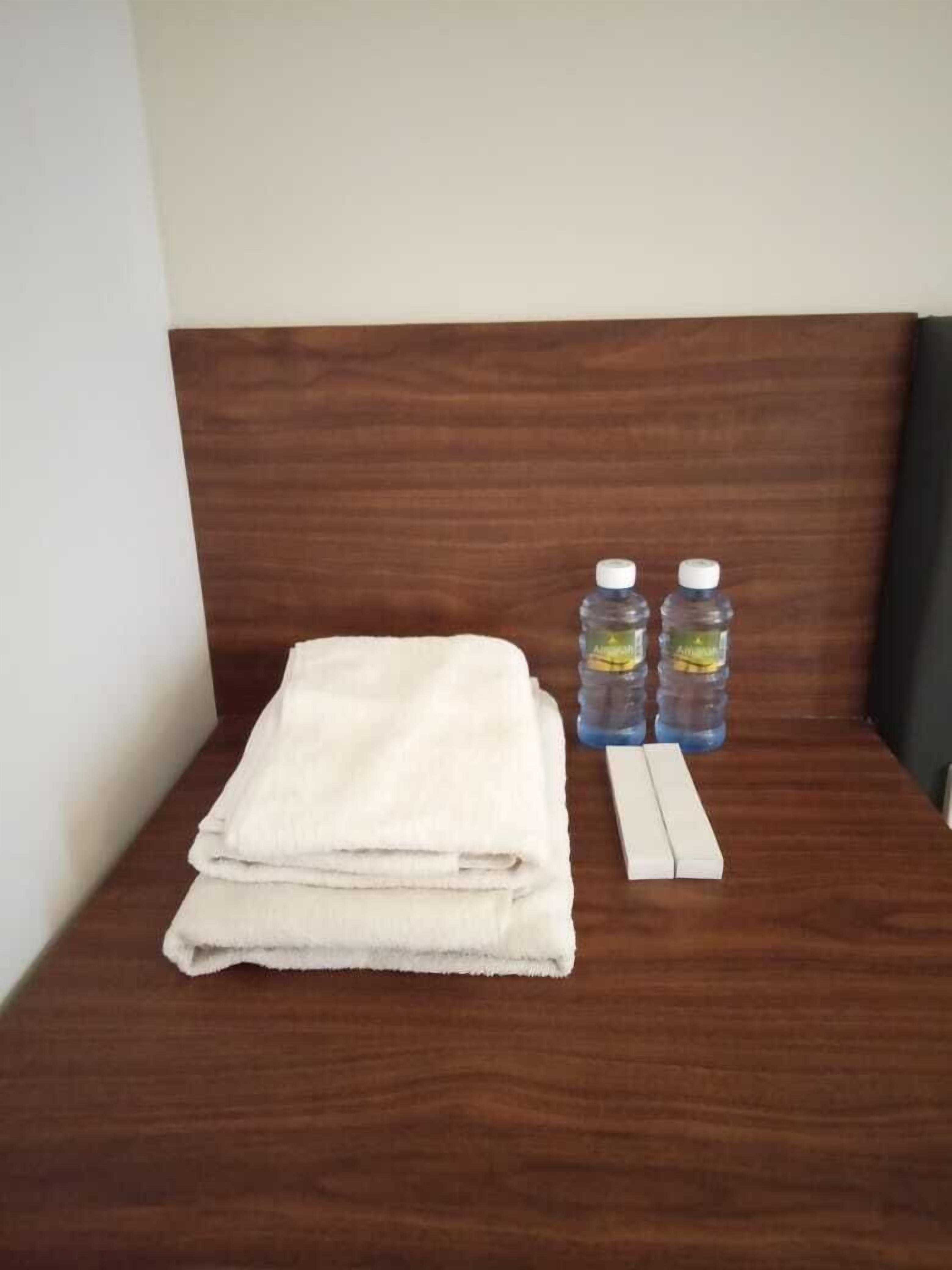 A neatly made bed with a folded white towel and two water bottles on a wooden headboard.