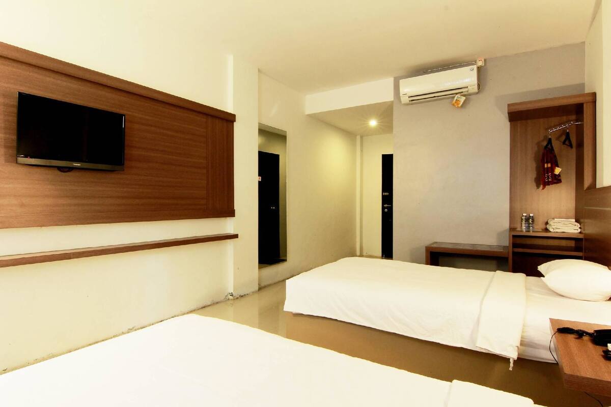 A hotel room with a bed, a TV mounted on the wall, a wardrobe, and a small table with a phone.