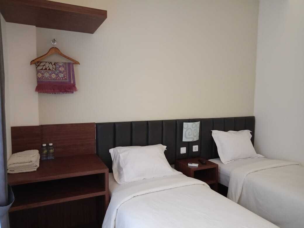 A hotel room with two beds, a wooden nightstand, a small table, and a hanging towel.