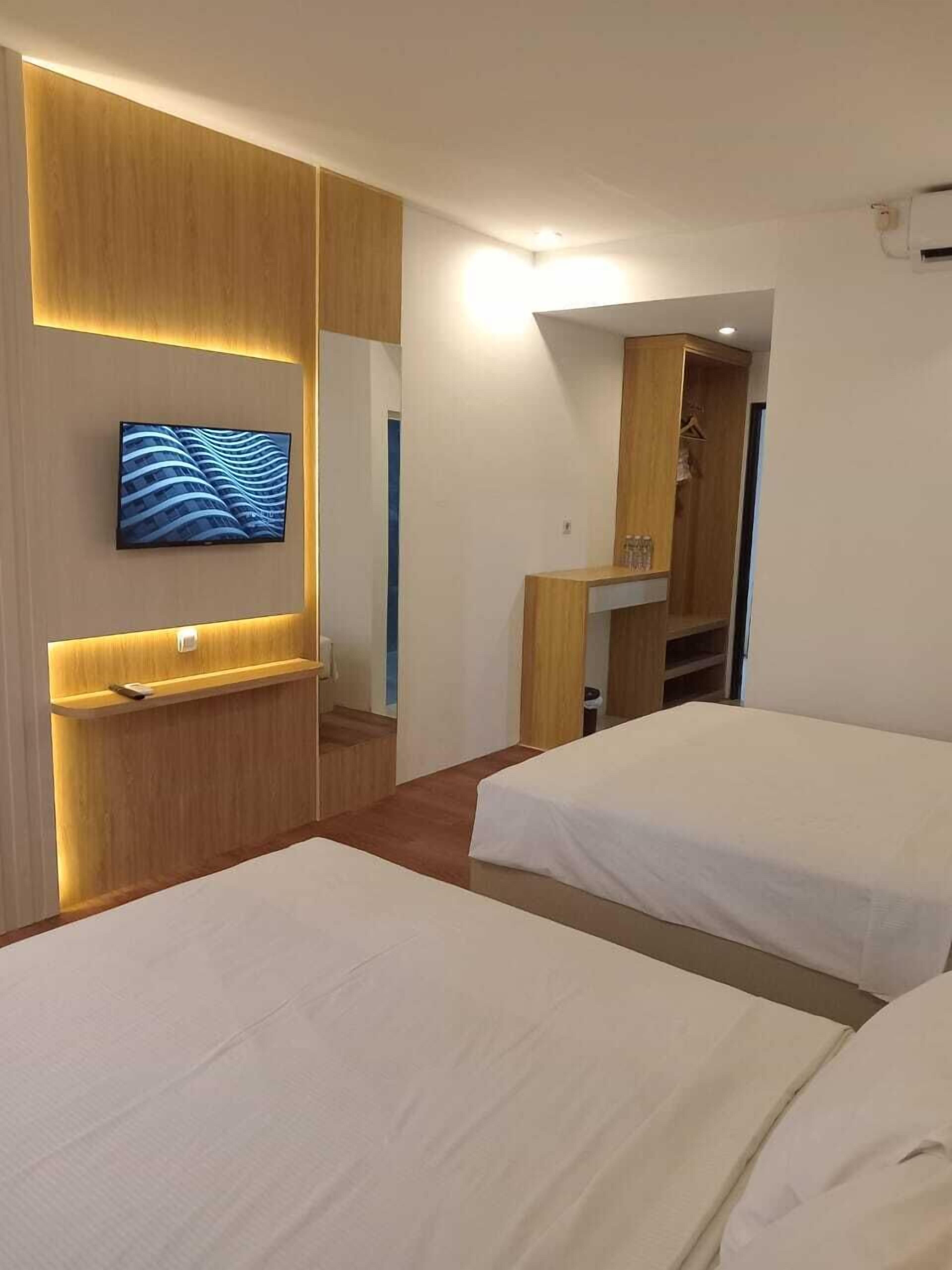 Ein Hotelzimmer mit zwei Betten, einem an der Wand befestigten Fernseher und einem Holzschrank mit Spiegel.