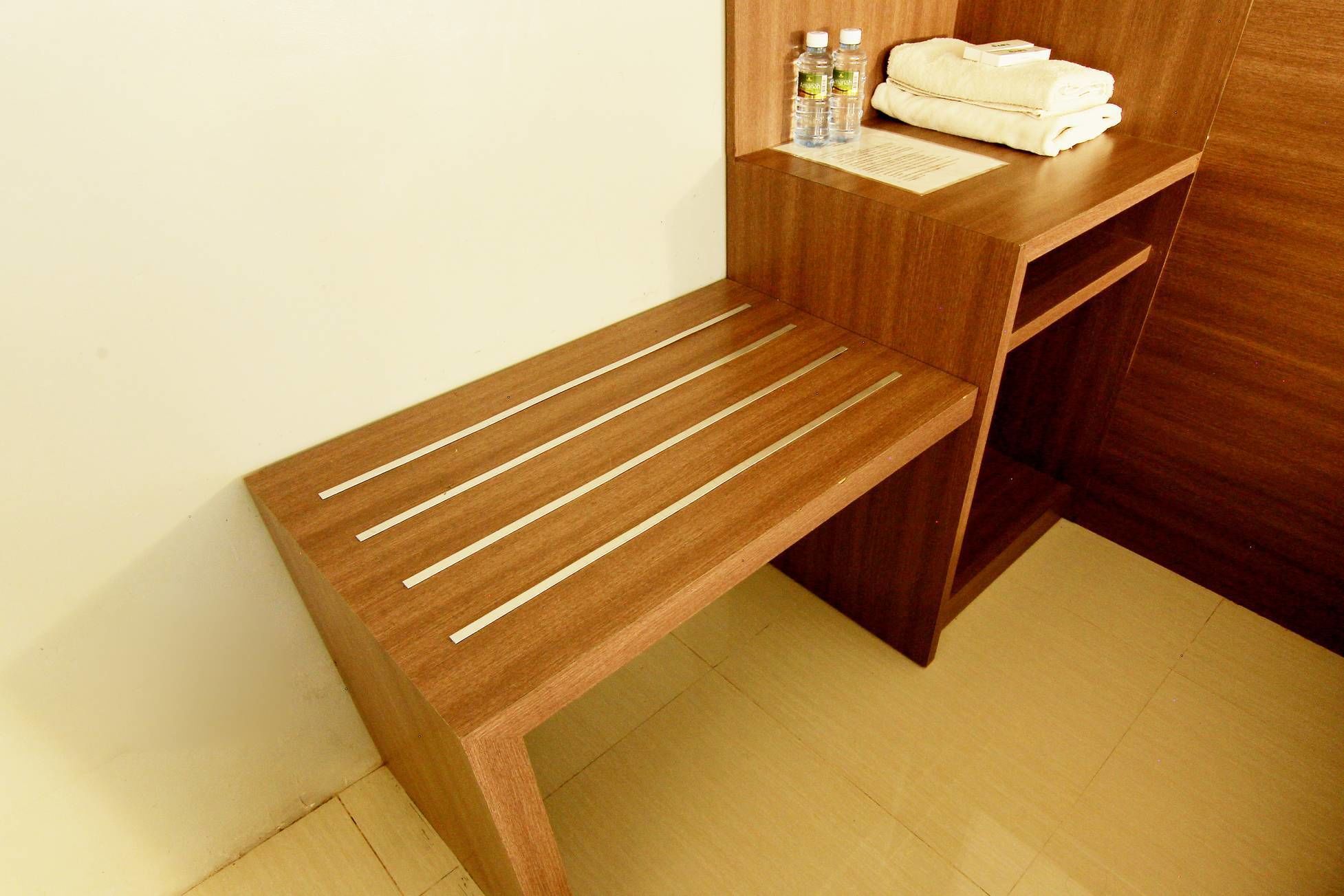 Um banco de madeira com assentos em ripas e uma mesa de madeira com uma toalha e artigos de higiene.
