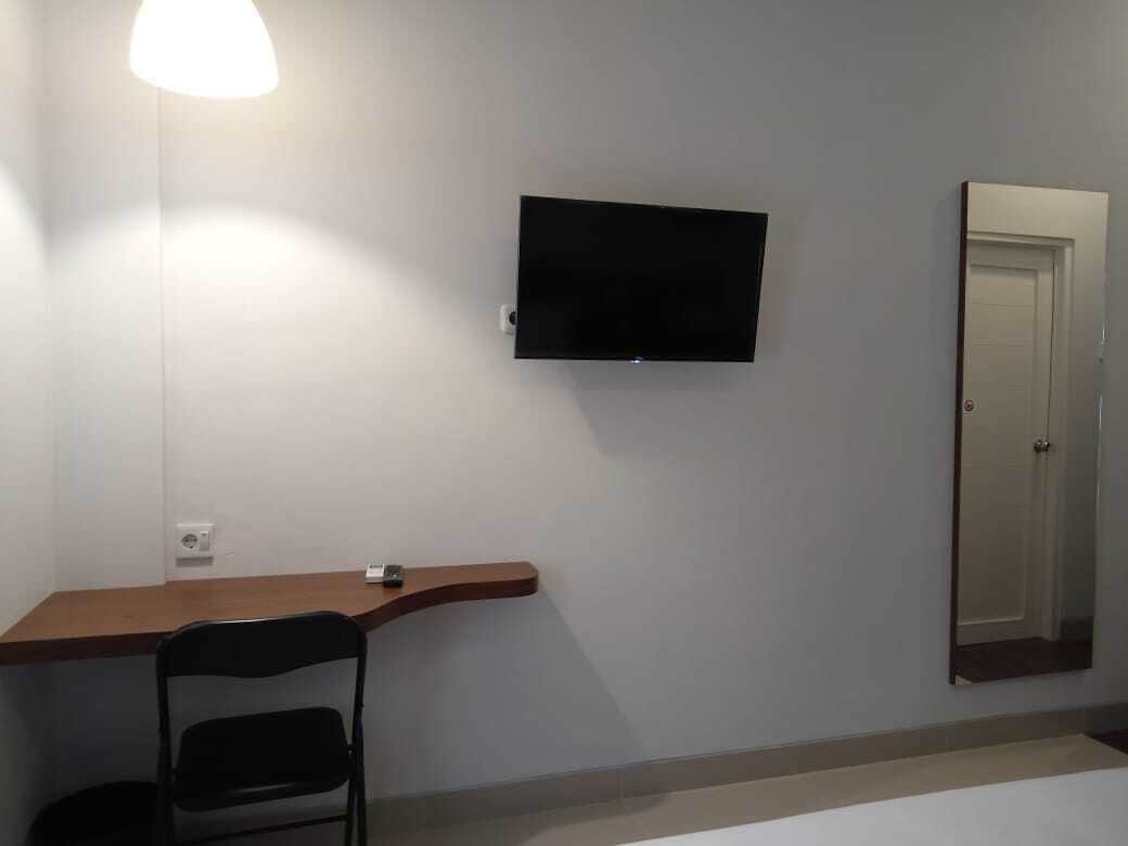 A room with a flat-screen TV mounted on the wall, a wooden desk, a black chair, and a door.