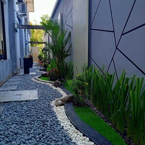 A narrow pathway with pebbles and small plants, flanked by walls with geometric patterns and air conditioning units. - Alzara Hotel (Wonosari)